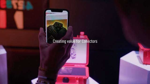 A visitor views artwork through a phone beside a glowing pink exhibition case